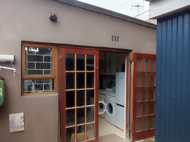Rear exterior view of the cottage featuring french doors leading into the kitchen area, with adjacent corrugated metal structure and security window bars.