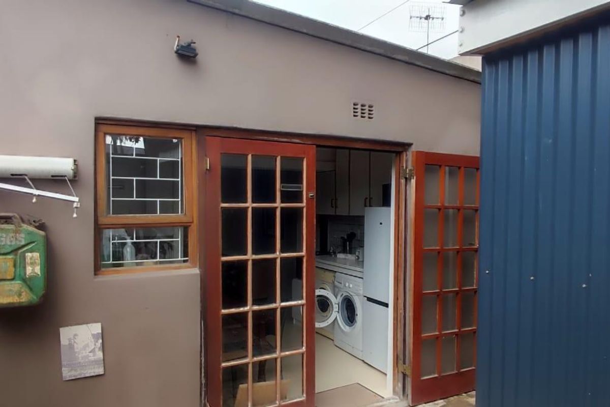 Rear exterior view of the cottage featuring french doors leading into the kitchen area, with adjacent corrugated metal structure and security window bars.