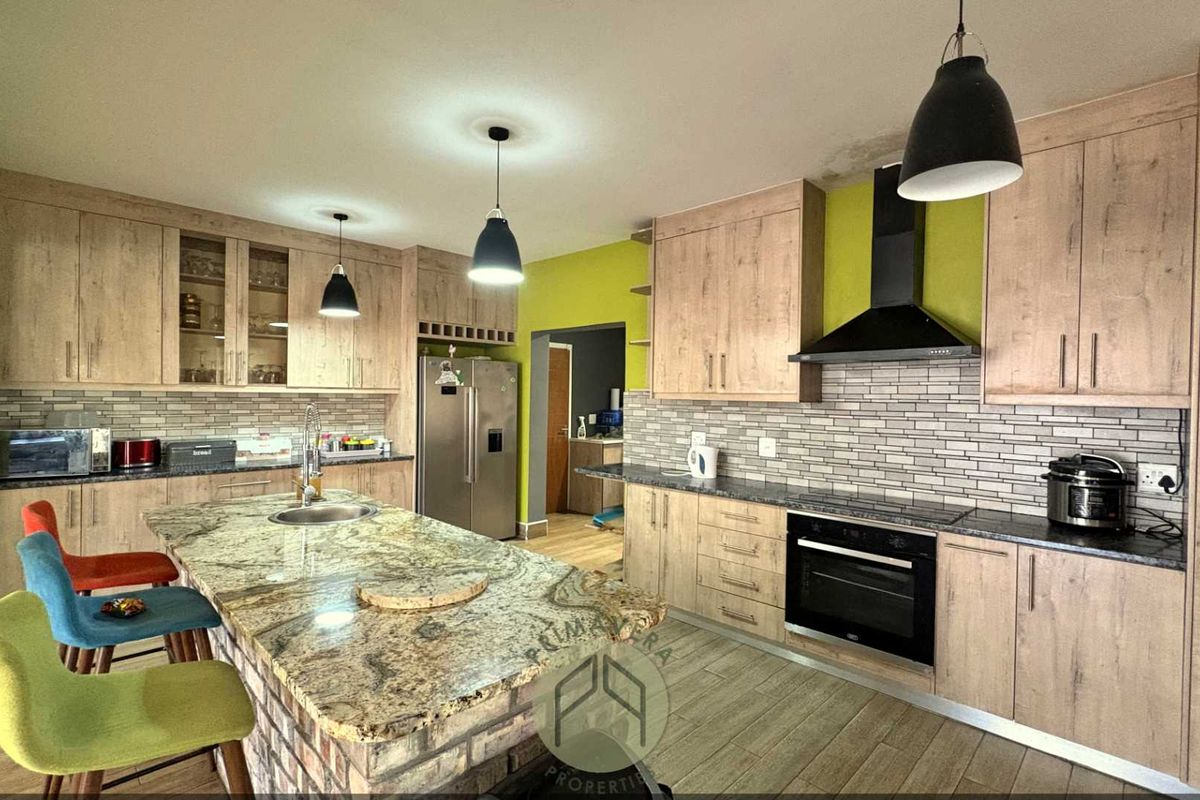 Spacious kitchen featuring light wood cabinetry, granite countertops, a central island with a prep sink, and a built-in oven with an extractor fan.