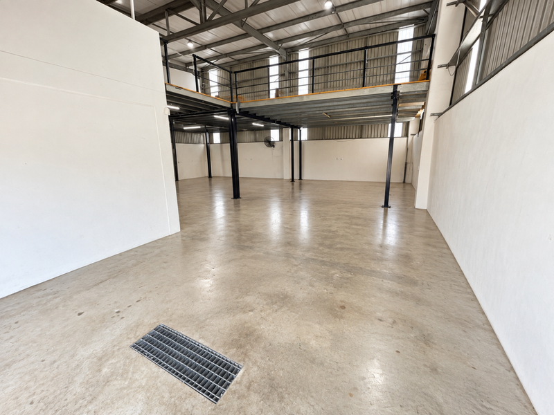 Spacious industrial utility area featuring a mezzanine level, exposed steel roof trusses, concrete flooring, and integrated floor drainage.