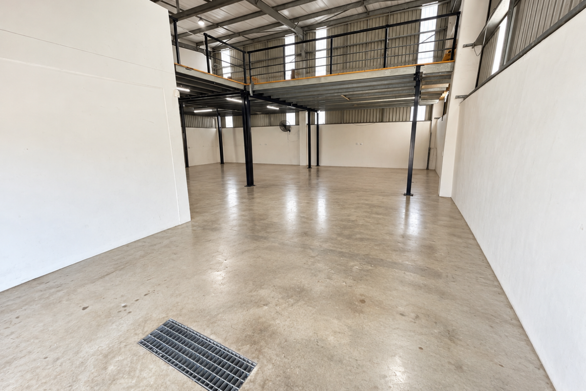 Spacious industrial utility area featuring a mezzanine level, exposed steel roof trusses, concrete flooring, and integrated floor drainage.