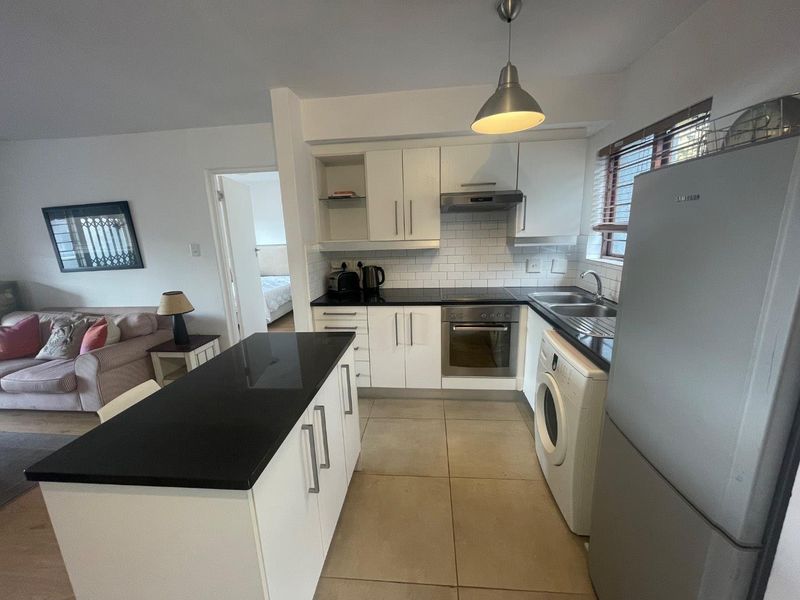 Open-plan kitchen featuring white cabinetry, black granite countertops, subway tile backsplash, and a functional kitchen island, seamlessly connected to the living area.