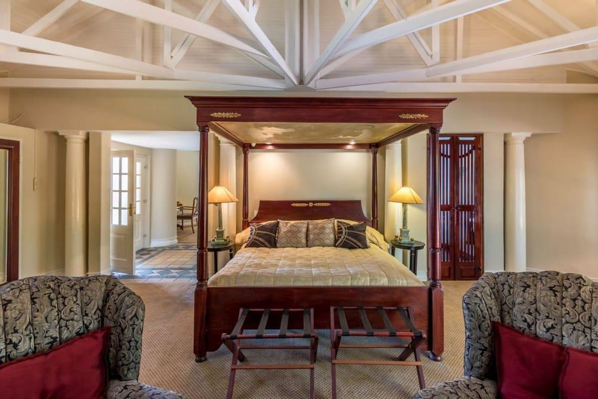 Spacious bedroom featuring a high vaulted ceiling with exposed white trusses, decorative columns, and integrated wooden cabinetry.