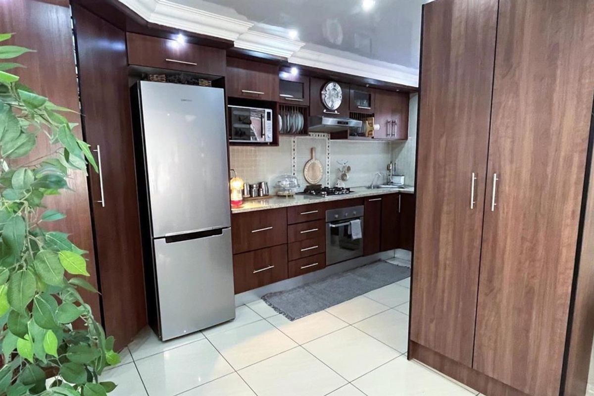A well-maintained kitchen featuring dark wood cabinetry, integrated oven and hob, tiled flooring, and ample storage space with a modern finish.