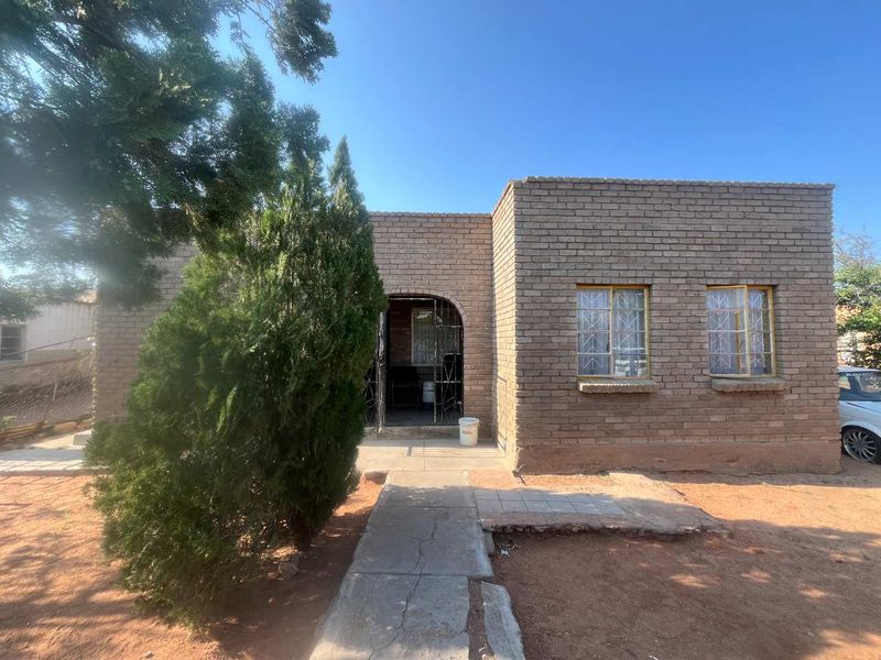 Front elevation of a face brick house featuring security gates and bars, with a concrete walkway leading to the entrance.