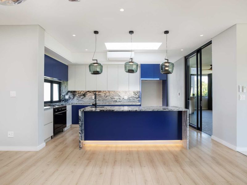 Modern kitchen featuring a central island with stone countertops, two-tone cabinetry, integrated lighting, and a skylight, opening onto an adjacent living space.