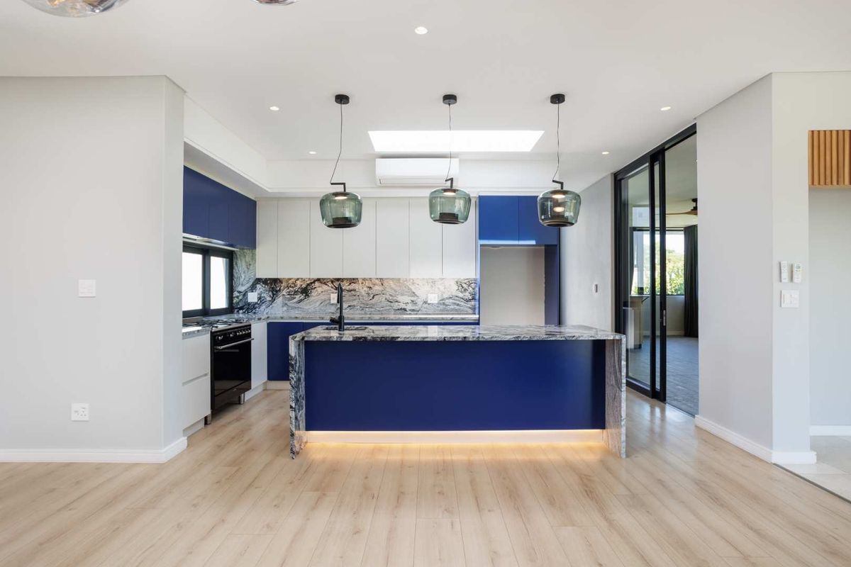 Modern kitchen featuring a central island with stone countertops, two-tone cabinetry, integrated lighting, and a skylight, opening onto an adjacent living space.