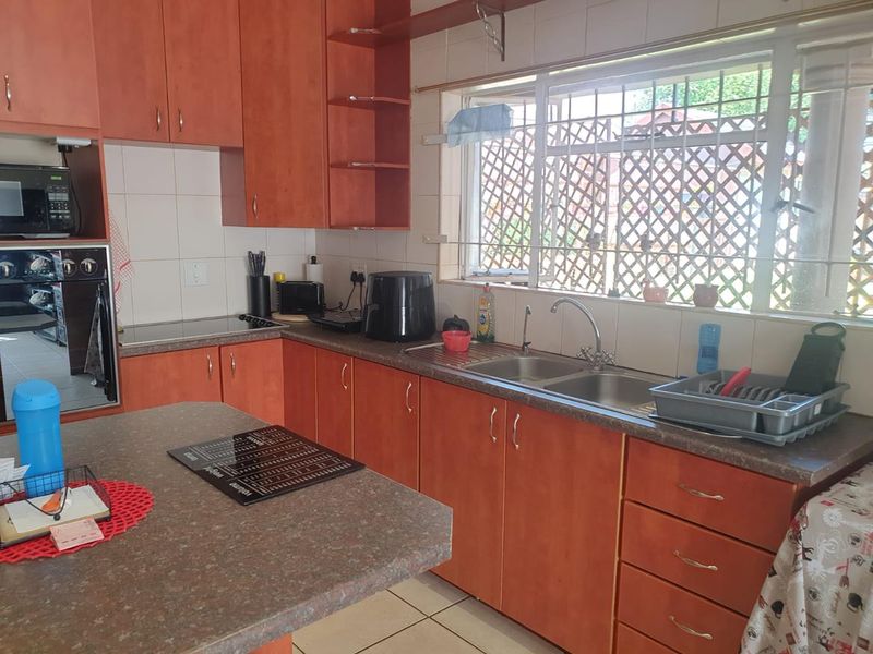 A functional kitchen featuring wood-tone cabinetry, laminate countertops, a double stainless steel sink, and built-in cooking appliances with a tiled backsplash.