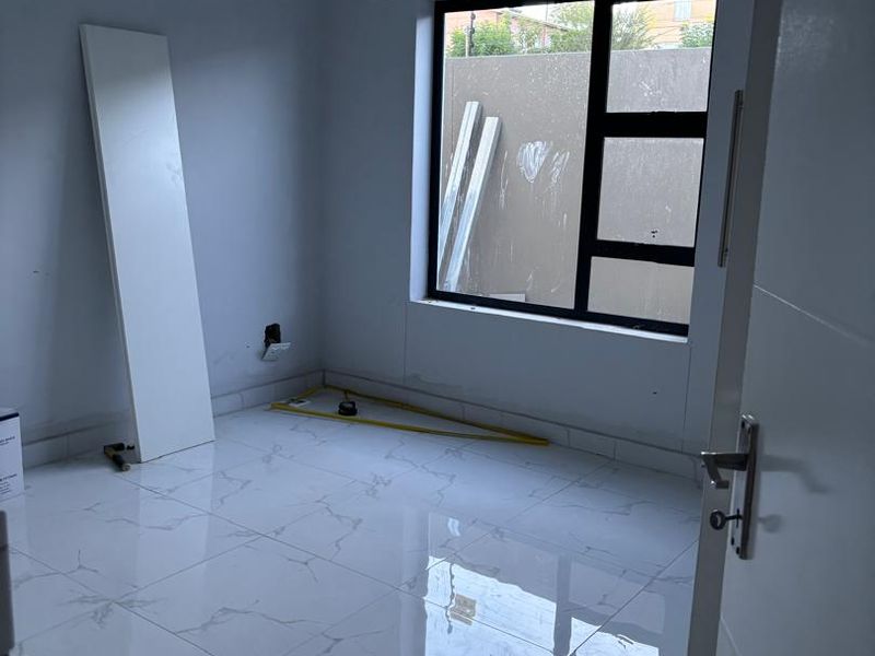 An empty bedroom featuring modern white marble-look floor tiles and a large aluminium-framed window, currently undergoing final finishing touches.