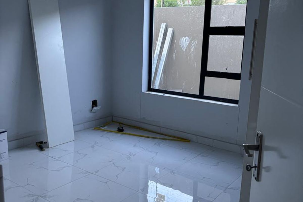 An empty bedroom featuring modern white marble-look floor tiles and a large aluminium-framed window, currently undergoing final finishing touches.