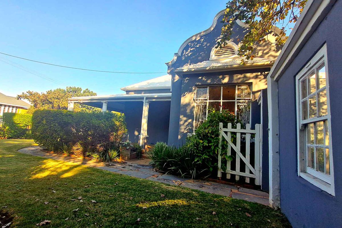 A charming rear exterior view of a house featuring a gabled roof, covered patio, and a well-maintained garden with a stone pathway.