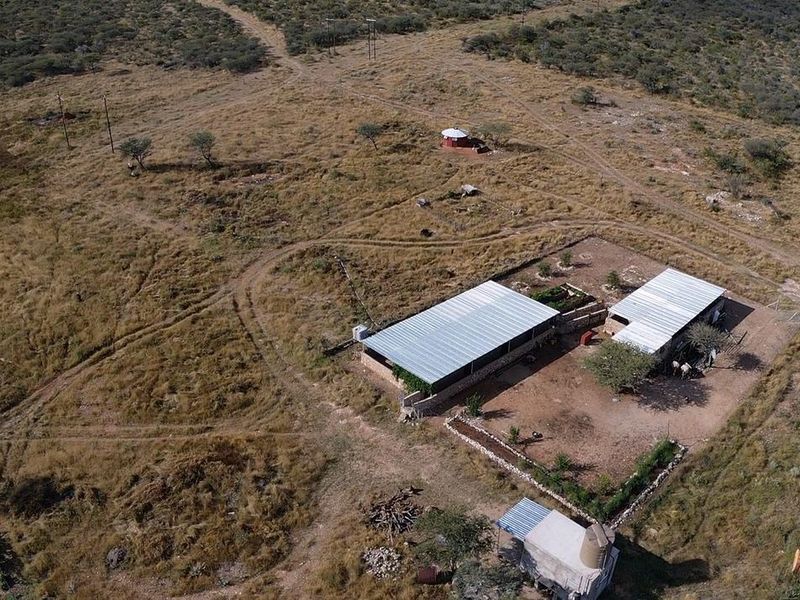Aerial view of a rural farm property featuring multiple structures with corrugated metal roofs, fenced enclosures, and surrounding dry landscape.