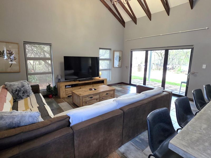 Spacious open-plan living area featuring high vaulted ceilings with exposed timber beams, tiled flooring, and large sliding glass doors leading to the garden.