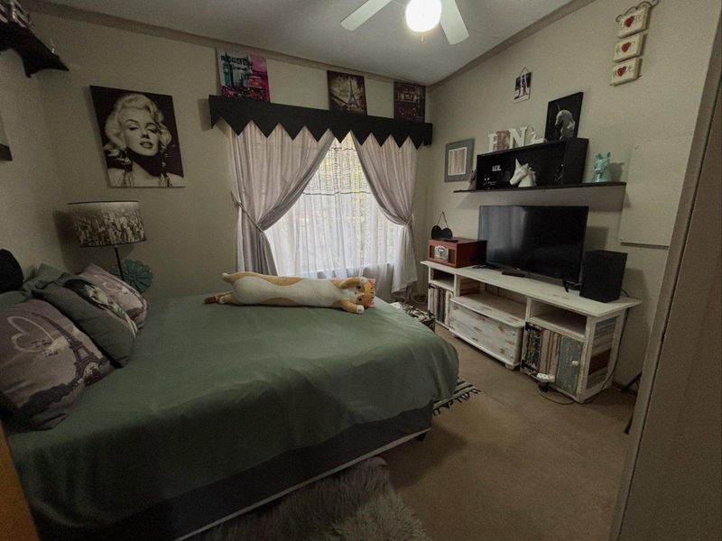 A standard bedroom featuring a ceiling fan and window with curtains, providing a functional space for rest.
