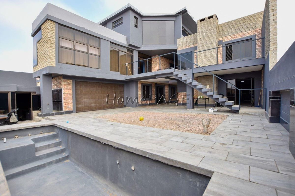 Rear view of a multi-level modern home featuring a paved patio, external staircase, balcony, and an unfinished swimming pool area.