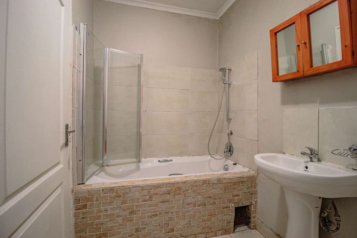 A functional bathroom featuring a bathtub with a glass shower screen, a pedestal basin, and a wall-mounted wooden medicine cabinet.