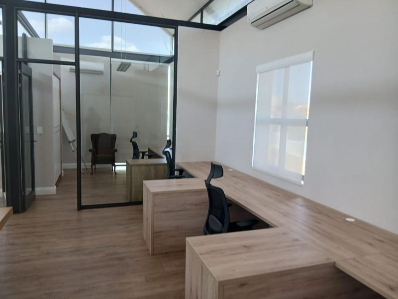 Modern office space featuring built-in wooden desks, glass partitioning, laminate flooring, and an integrated air conditioning unit.