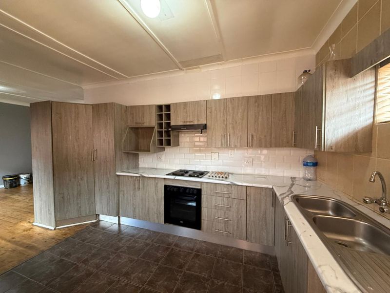 A functional kitchen featuring wood-look cabinetry, marble-effect countertops, built-in oven, gas hob, and a double bowl stainless steel sink with subway tile backsplash.