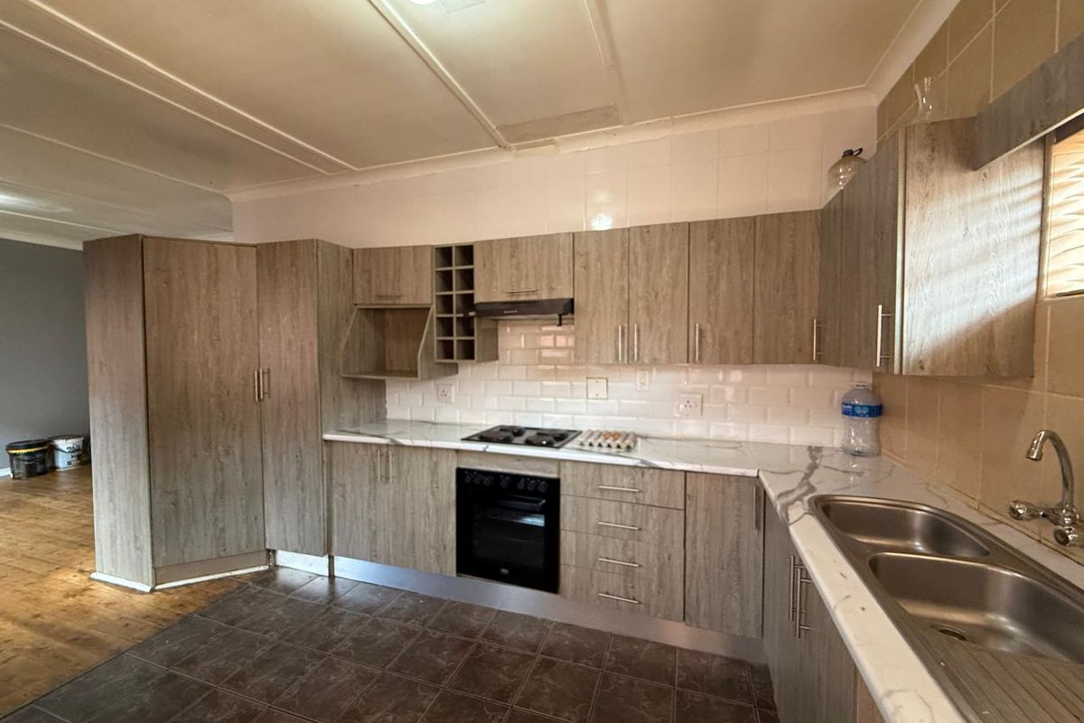 A functional kitchen featuring wood-look cabinetry, marble-effect countertops, built-in oven, gas hob, and a double bowl stainless steel sink with subway tile backsplash.