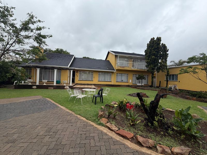 Spacious double-story family home featuring a tiled roof, covered patio, upper-level balcony, and a large landscaped garden with a paved driveway.