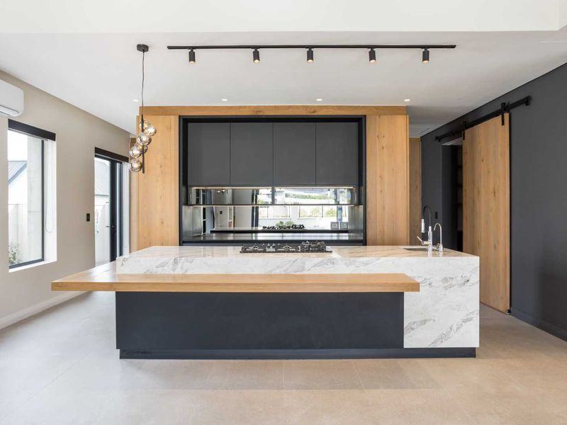 Modern kitchen featuring a large marble-topped island with integrated gas hob, sleek dark cabinetry, wood accents, and high-end track lighting.