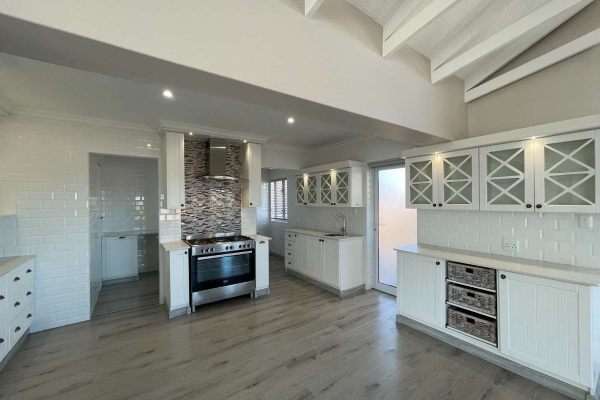 Modern, bright kitchen featuring white cabinetry, subway tile backsplash, stainless steel gas stove, and exposed white ceiling beams with laminate flooring.