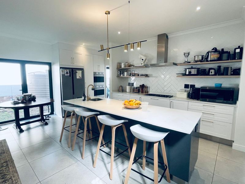 Modern kitchen featuring a large central island with quartz countertops, herringbone backsplash, built-in appliances, and stylish pendant lighting.