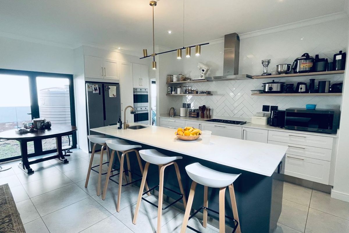 Modern kitchen featuring a large central island with quartz countertops, herringbone backsplash, built-in appliances, and stylish pendant lighting.