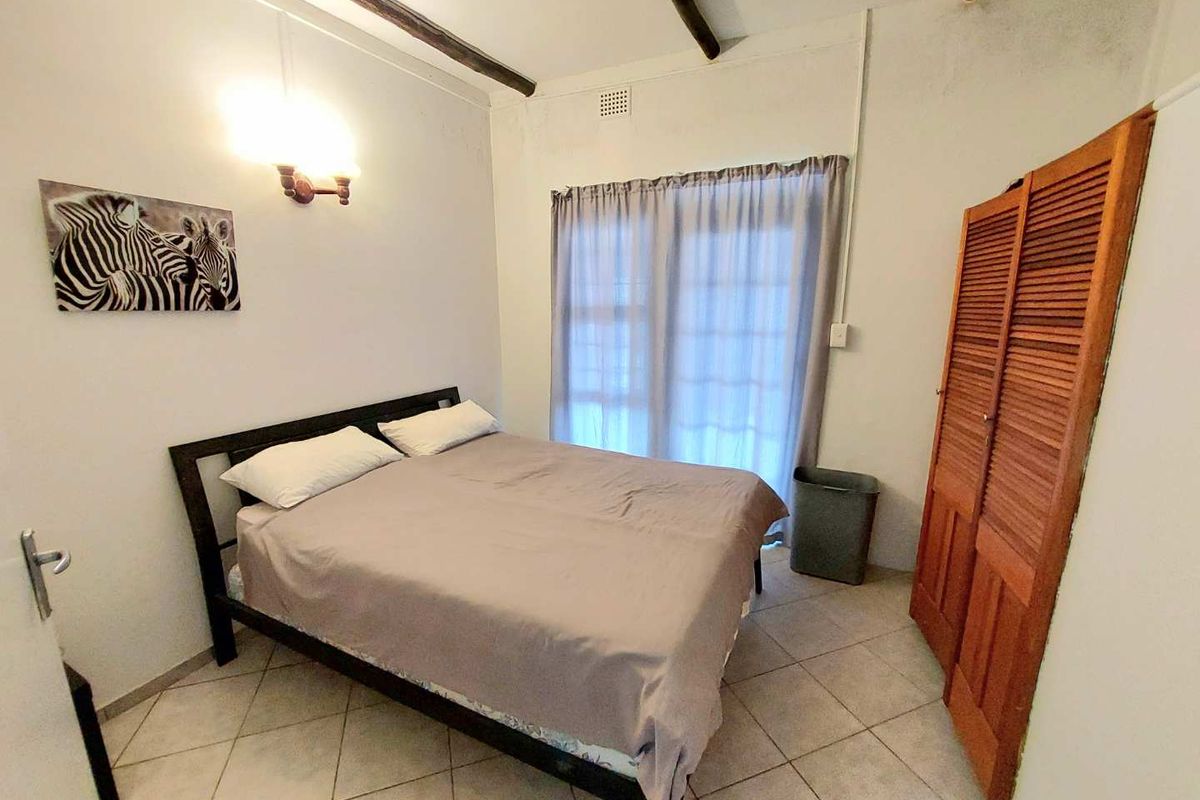 A bedroom featuring tiled flooring, exposed ceiling beams, and built-in wooden closet doors with access to an outdoor area through sliding glass doors.