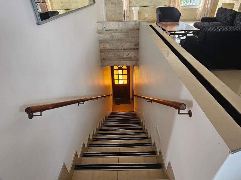A well-lit interior staircase featuring tiled steps with non-slip strips, a wooden handrail, and a view leading down to an entrance door.