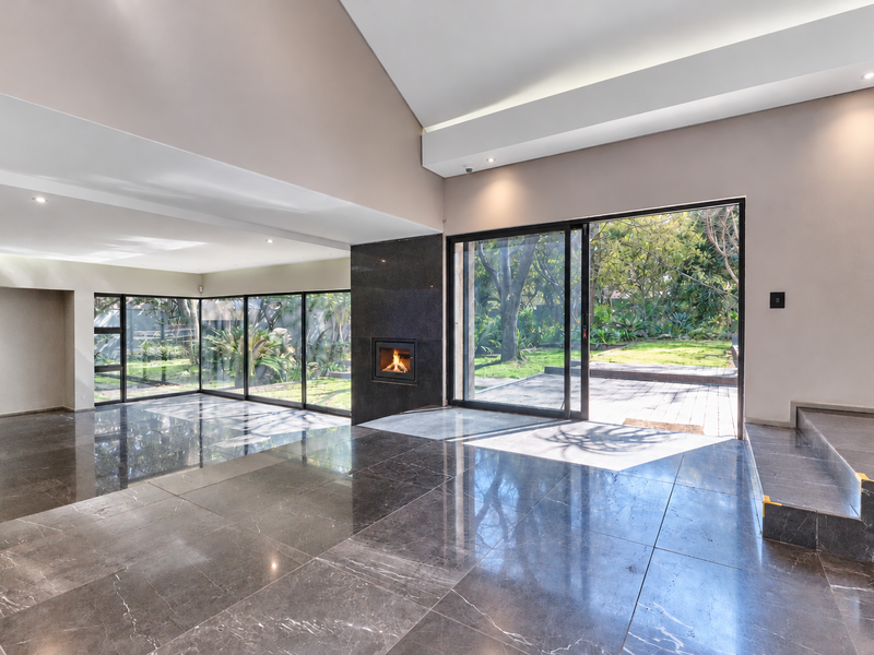 Spacious open-plan living area featuring polished marble flooring, a modern built-in fireplace, and large sliding glass doors opening to a lush garden.