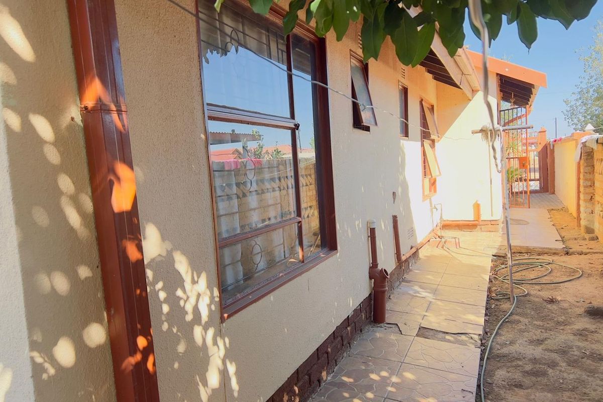 Side exterior view of the house featuring a tiled walkway, metal window frames with security bars, and exposed drainage pipes along the wall.