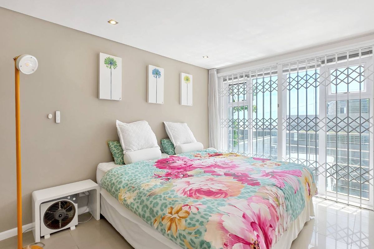A bright bedroom featuring tiled flooring, recessed downlights, and a sliding glass door with an integrated security gate leading to an outdoor area.