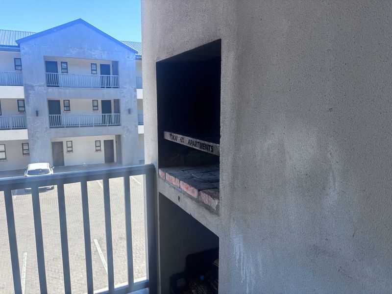 A balcony featuring a built-in braai and metal balustrade, overlooking the apartment complex courtyard and parking area.