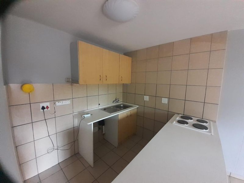 A compact kitchen featuring built-in cabinetry, a stainless steel sink, and an electric hob with tiled backsplash and flooring.