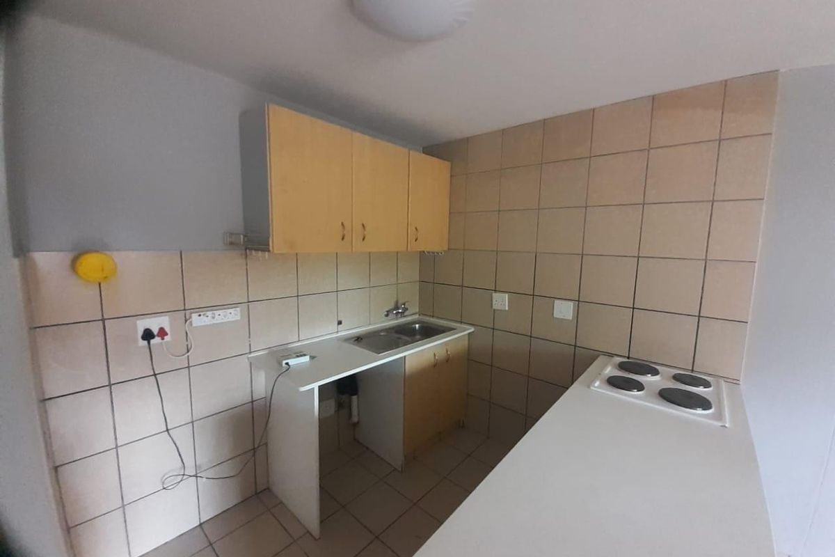 A compact kitchen featuring built-in cabinetry, a stainless steel sink, and an electric hob with tiled backsplash and flooring.