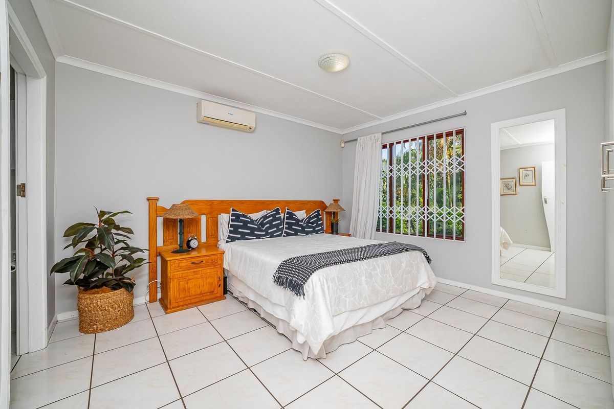 A well-lit bedroom featuring tiled flooring, a wall-mounted air conditioning unit, and security bars on the window.