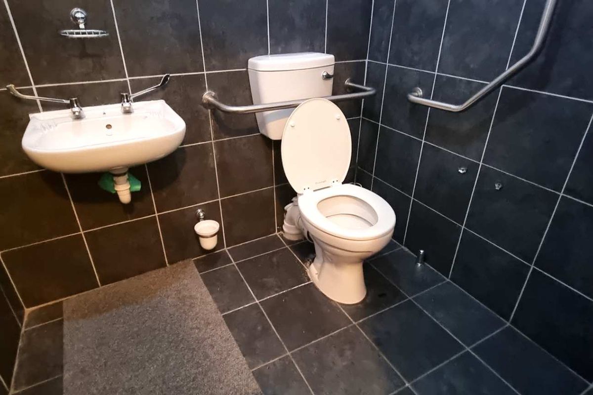 Accessible restroom featuring dark wall and floor tiling, a wall-mounted basin, and stainless steel grab rails for enhanced safety and utility.