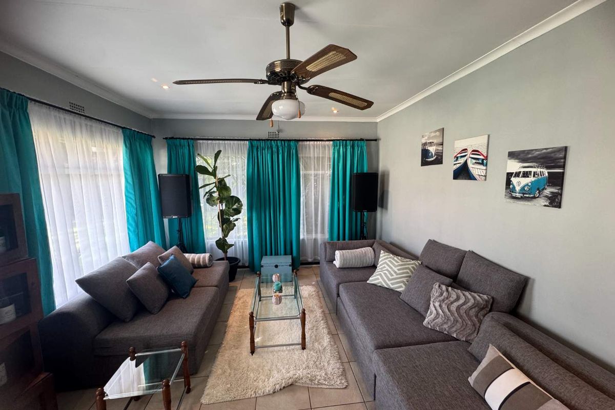 A comfortable living room featuring tiled flooring, a central ceiling fan, and large windows dressed with curtains, providing a bright and functional space.