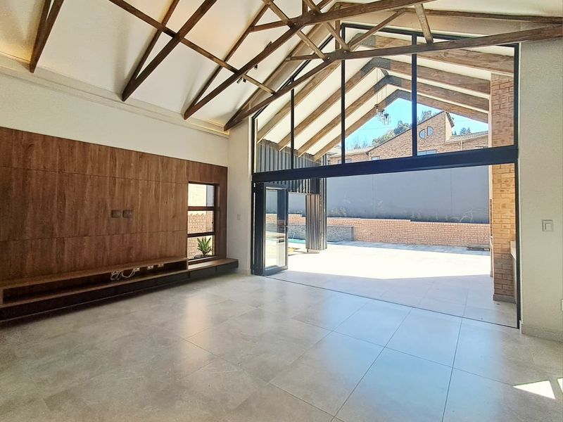 Spacious living area featuring vaulted ceilings with exposed timber trusses, large glass sliding doors opening to the patio, and modern built-in cabinetry.