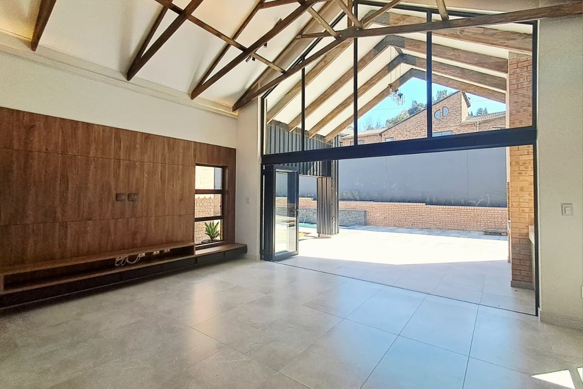 Spacious living area featuring vaulted ceilings with exposed timber trusses, large glass sliding doors opening to the patio, and modern built-in cabinetry.