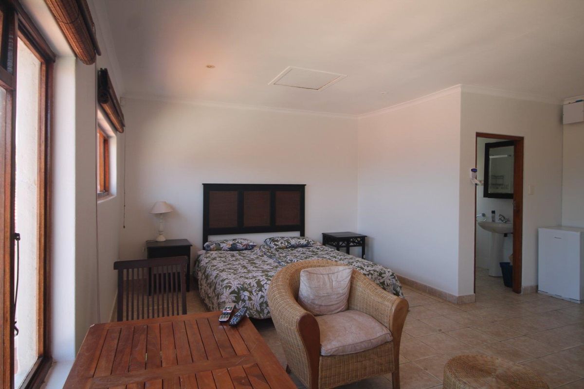 A bedroom featuring tiled flooring and an en-suite bathroom, with direct access to an outdoor area through large windows.