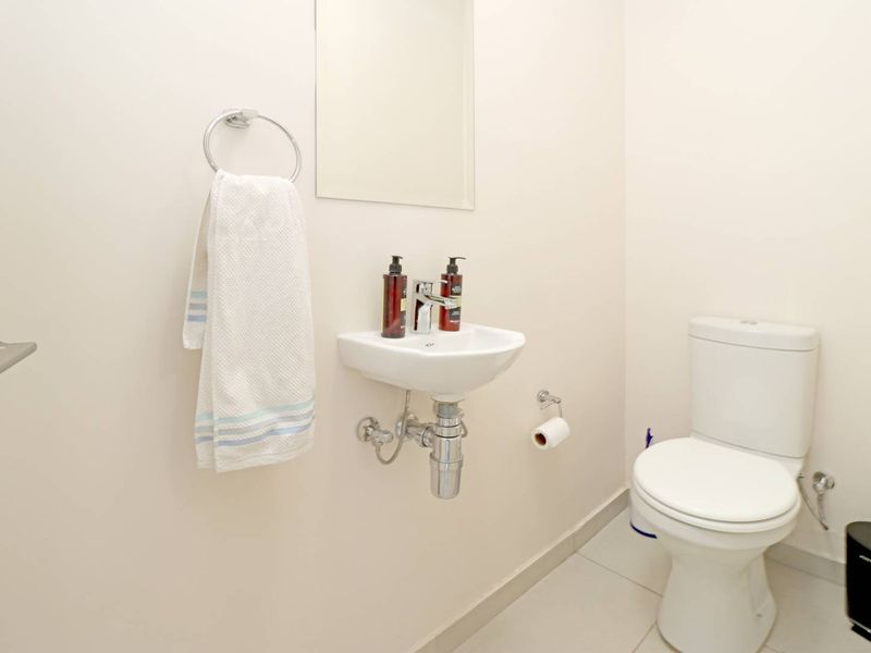 A clean and functional guest bathroom featuring a wall-mounted basin, modern toilet, and neutral tiled flooring.