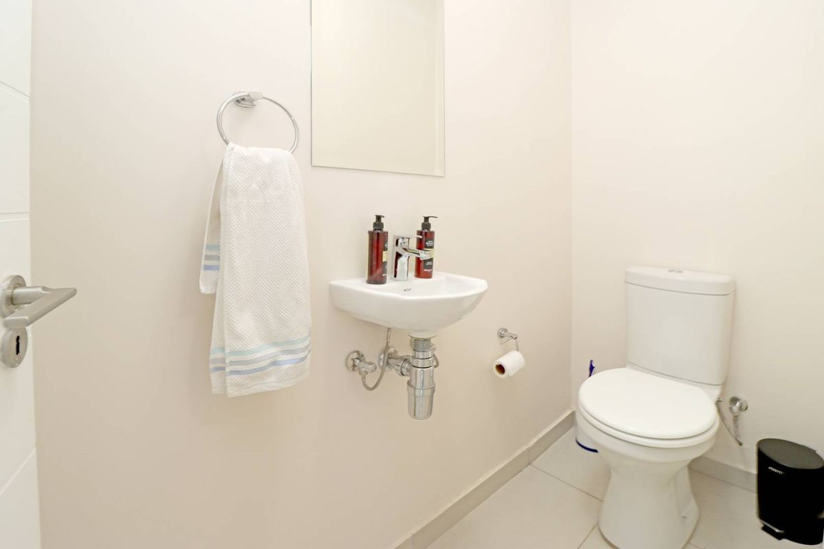 A clean and functional guest bathroom featuring a wall-mounted basin, modern toilet, and neutral tiled flooring.