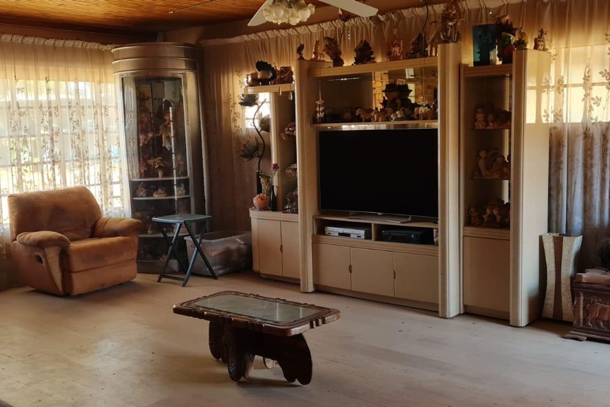 A living room featuring an exposed brick fireplace, timber ceiling, and ceiling fan, offering a traditional aesthetic with potential for modern updates.