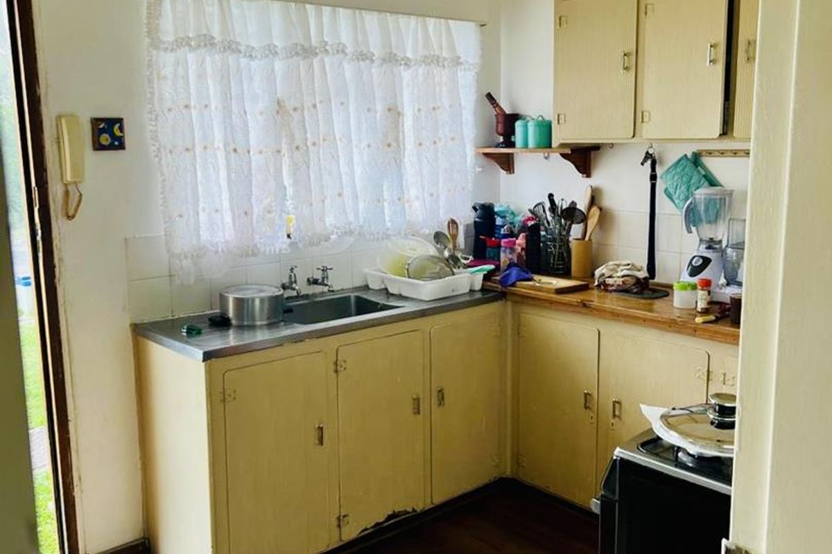 A compact, dated kitchen featuring original cabinetry, a stainless steel sink, and wood-look flooring, offering potential for a modern renovation.