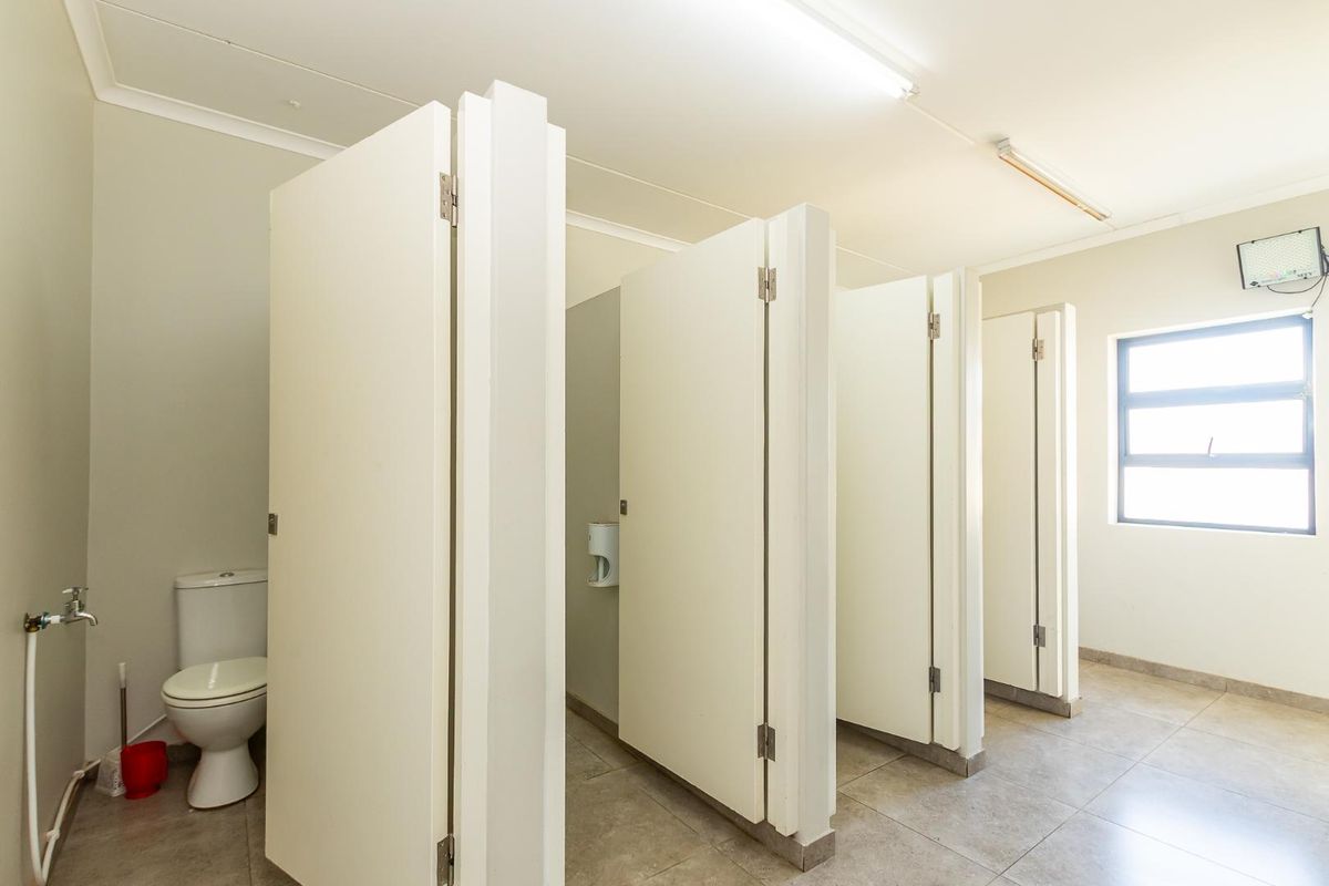 A functional office restroom featuring multiple toilet cubicles with privacy doors, tiled flooring, and a window for natural light.