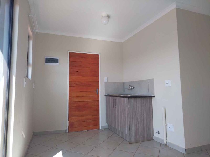 A clean and functional laundry area featuring tiled flooring, a single basin sink with laminate cabinetry, and a dedicated plumbing connection point.