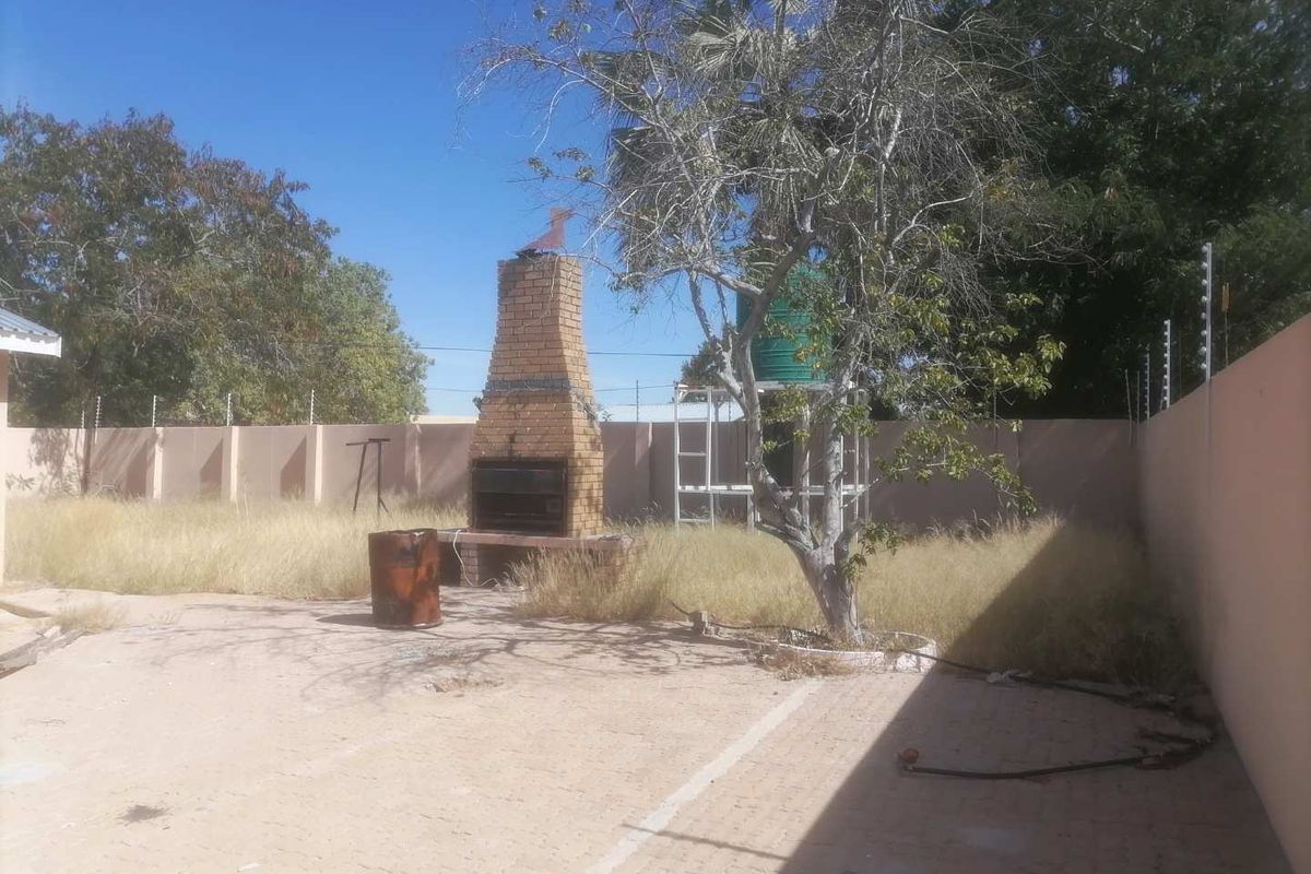 Rear garden area featuring a built-in brick braai, paved patio space, and perimeter wall with electric fencing.