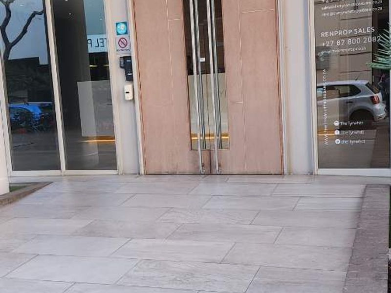 Modern apartment building entrance featuring large format floor tiles, double glass doors, and full-height glass paneling.